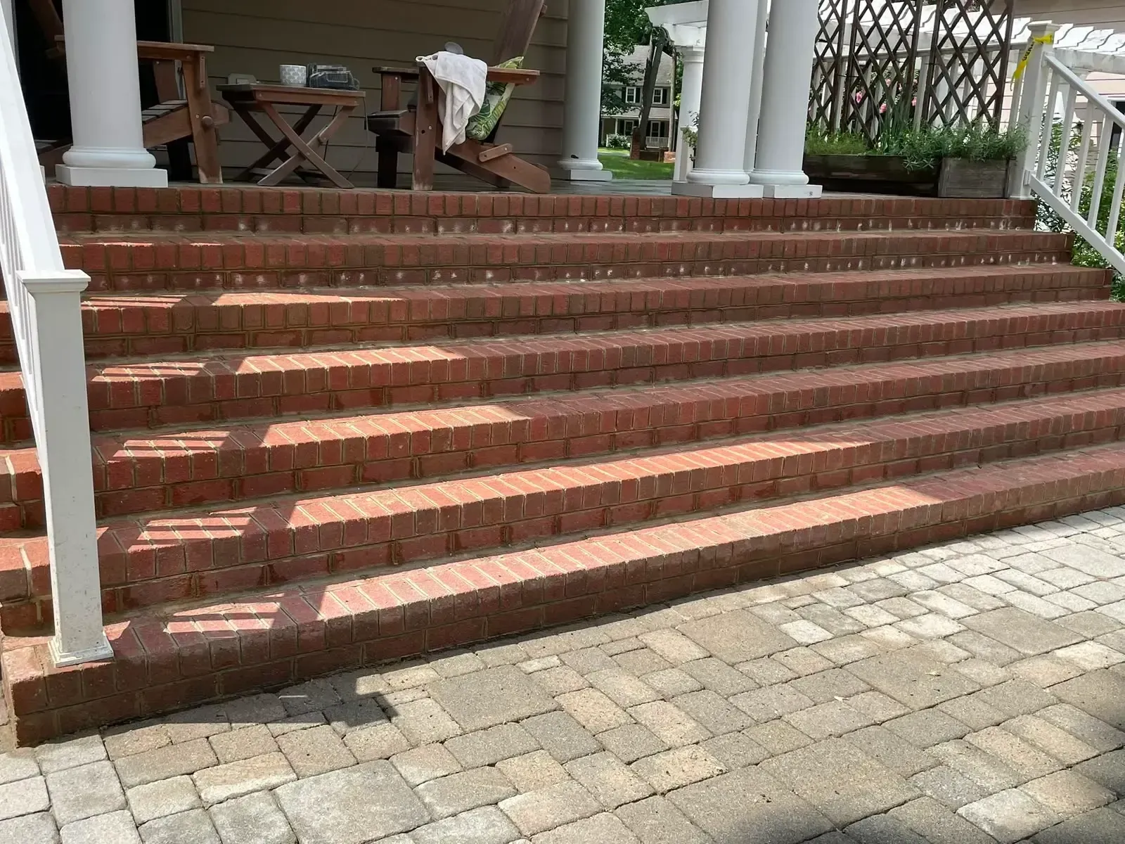 Red brick steps leading to a porch with white columns and a stone-paved walkway