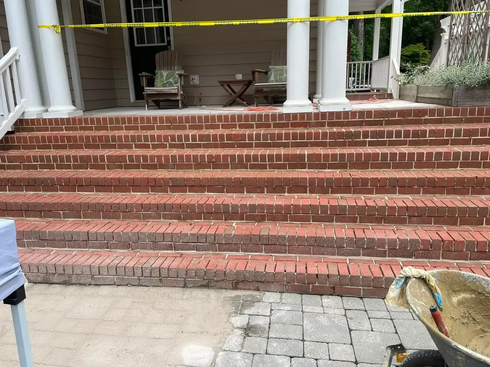 Brick steps blocked by yellow caution tape at a building entrance with white columns.