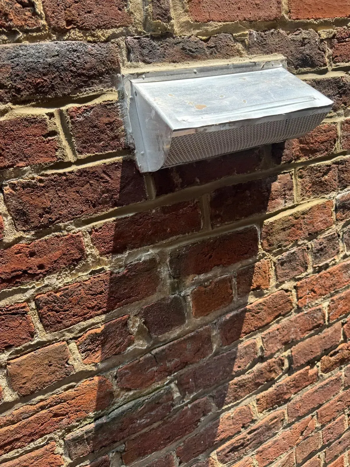 Brick wall with a small metal vent protruding from it