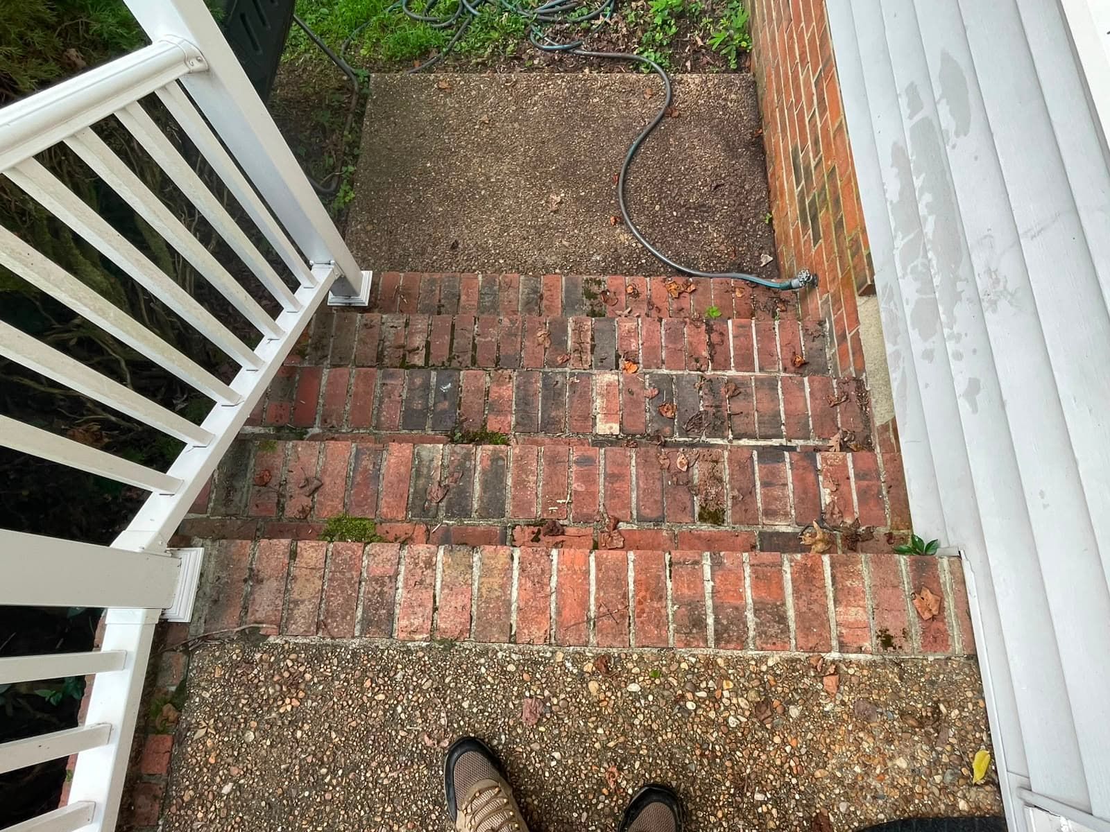Brick steps leading down to a gravel path beside white railing and house siding