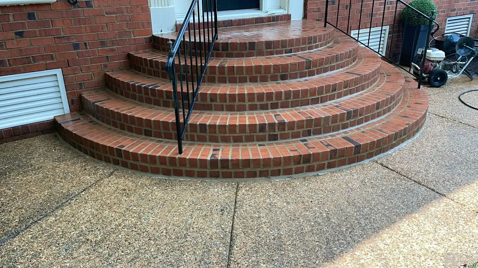 Brick steps with a black handrail leading to a white front door, beside a gravel driveway.