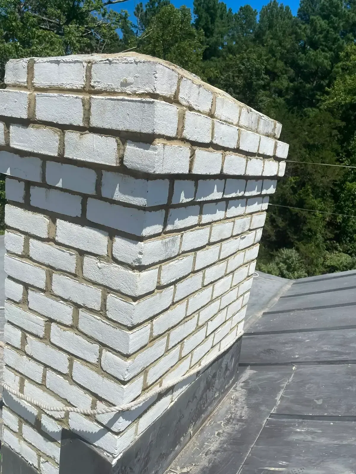White brick chimney stack on a rooftop with trees in the background