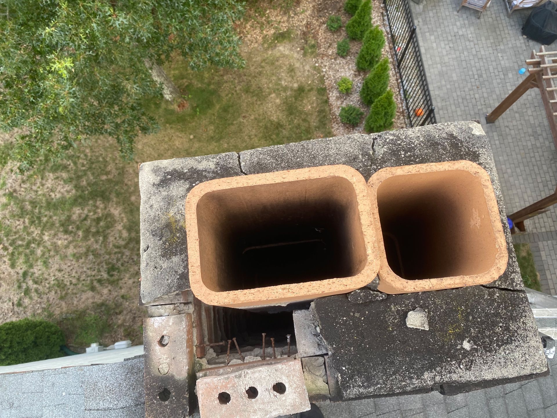 Two terracotta chimney flues on a rooftop beside a brick vent and gravel surface