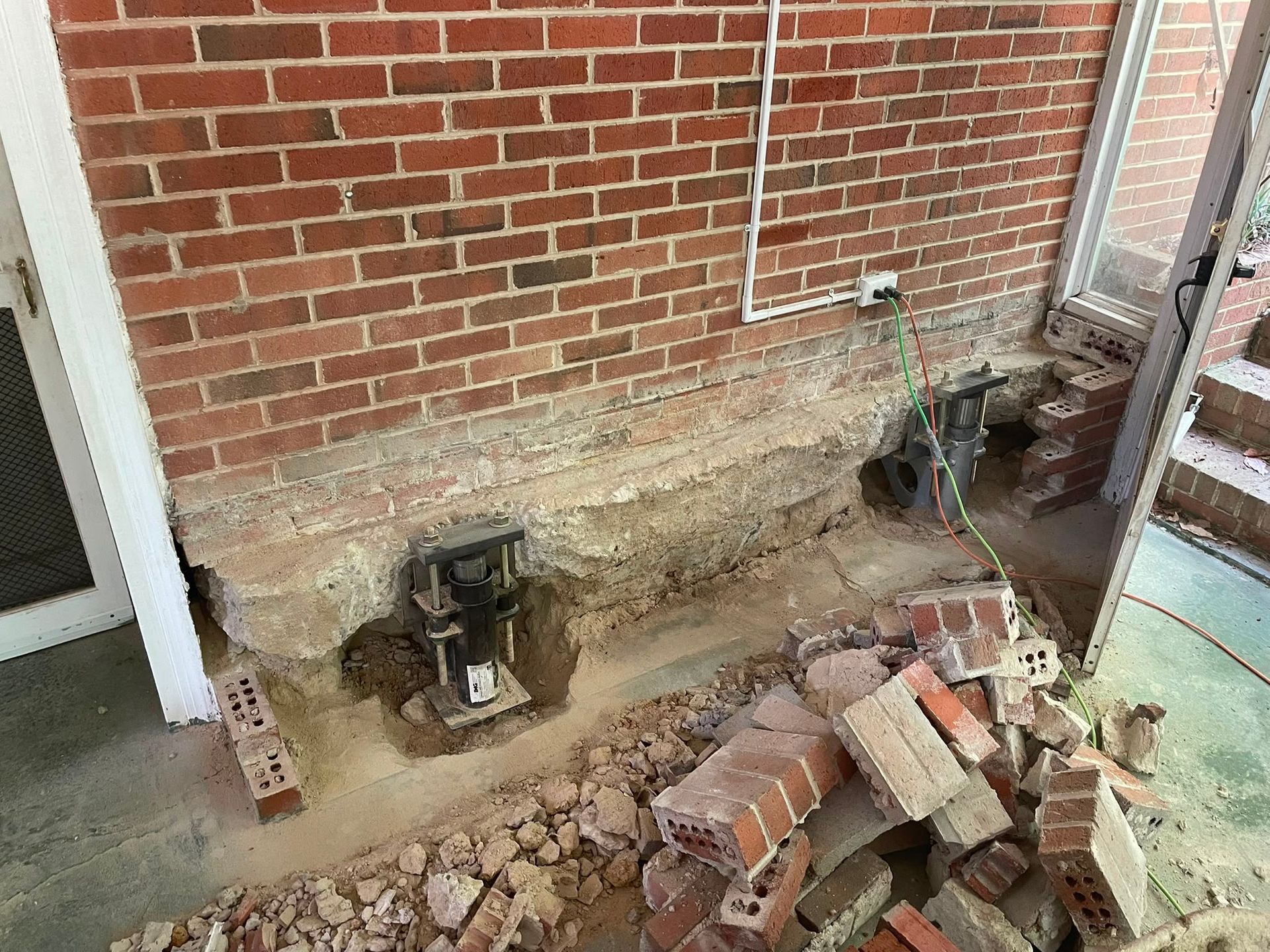 Broken brick foundation wall with exposed soil, a pipe, and a pile of loose bricks and debris.