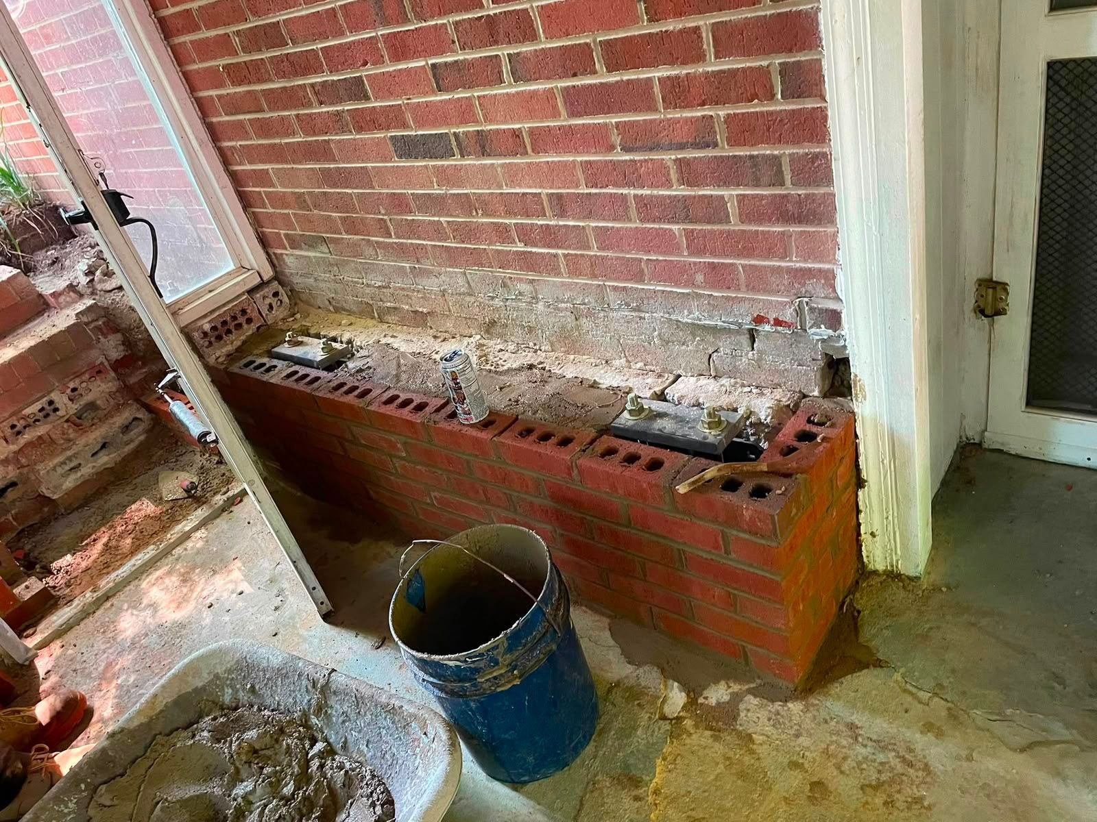 Partially demolished brick porch with a blue bucket and debris on the floor