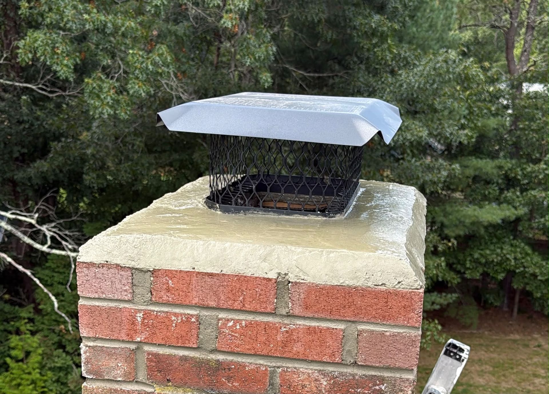 Brick chimney cap wrapped in a white tarp, with a small black vent on top against trees.