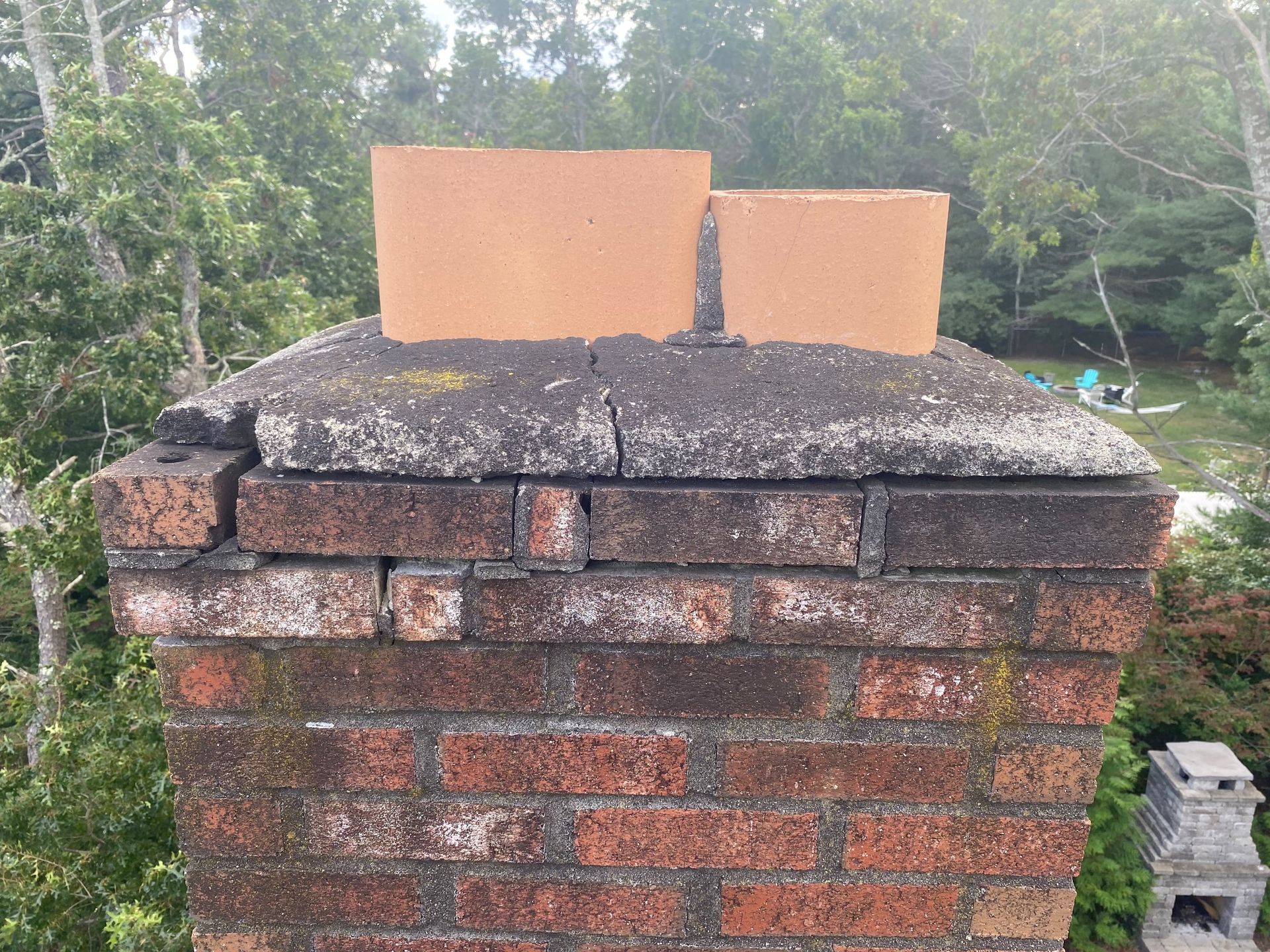 Brick chimney with two orange chimney caps against a leafy outdoor background