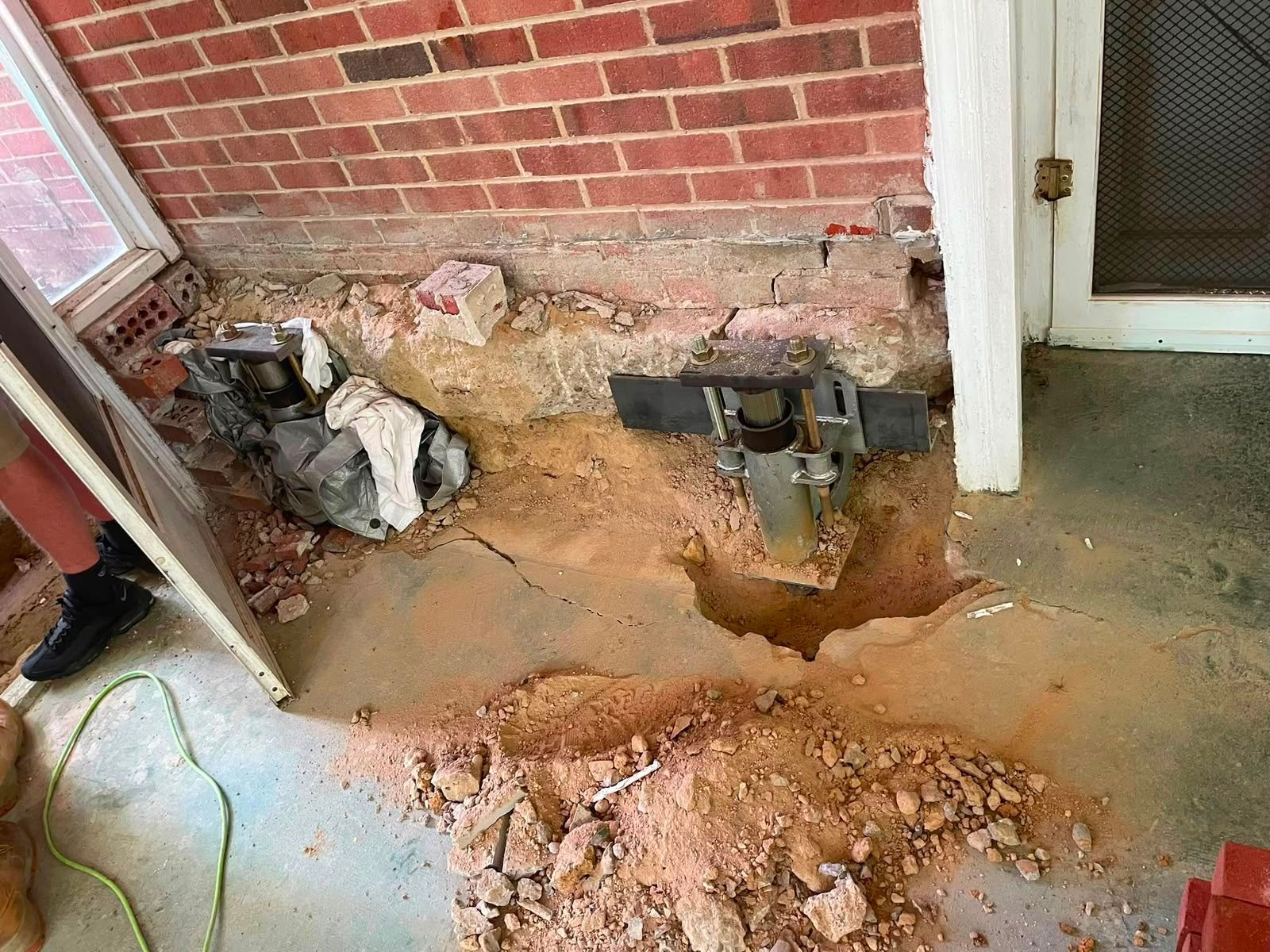 Damaged concrete floor with broken brick wall, exposed soil, and debris by a doorway