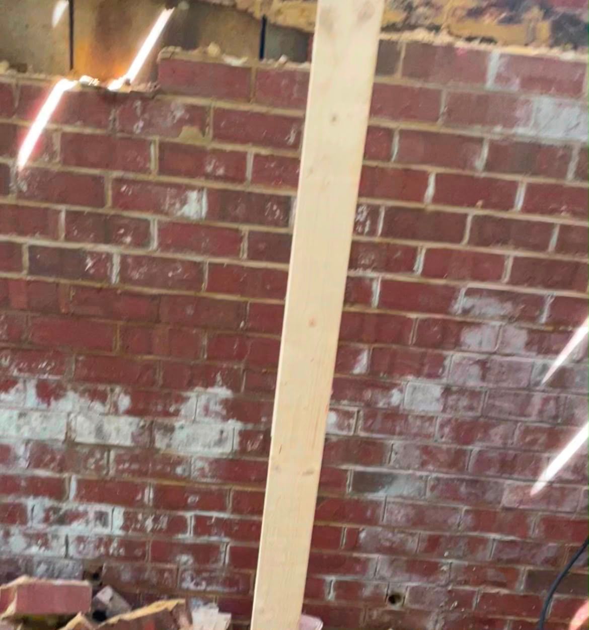 Interior with exposed red brick wall, a beige vertical beam, and a damaged ceiling with light peeking through.