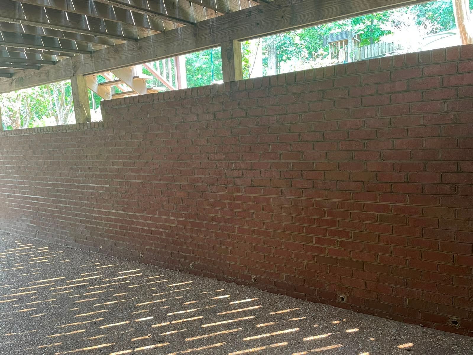 Red brick wall under a concrete roof, with sunlight casting striped shadows on the ground.