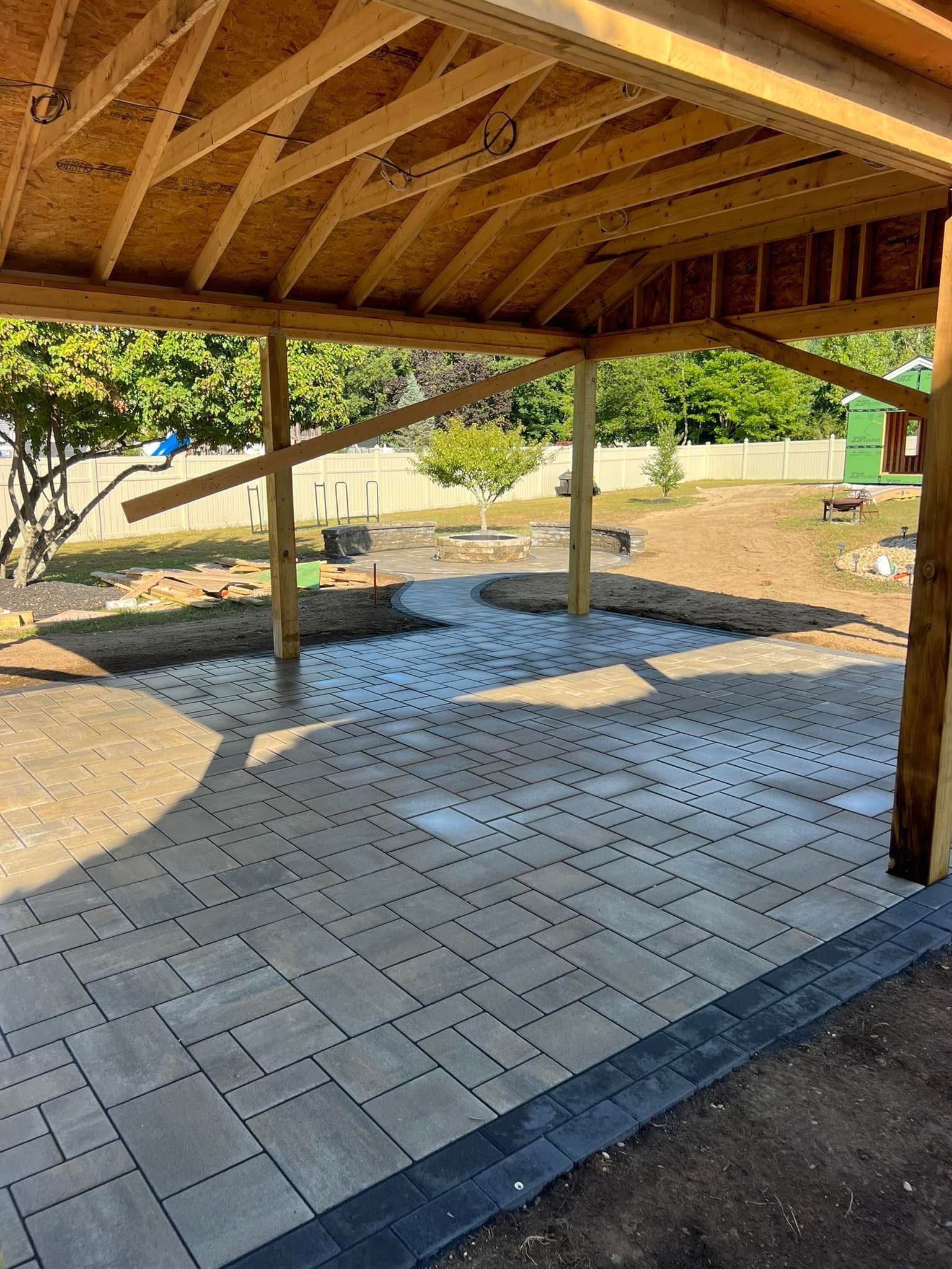 Covered patio with wooden roof, brick pavers, and sunny yard beyond.