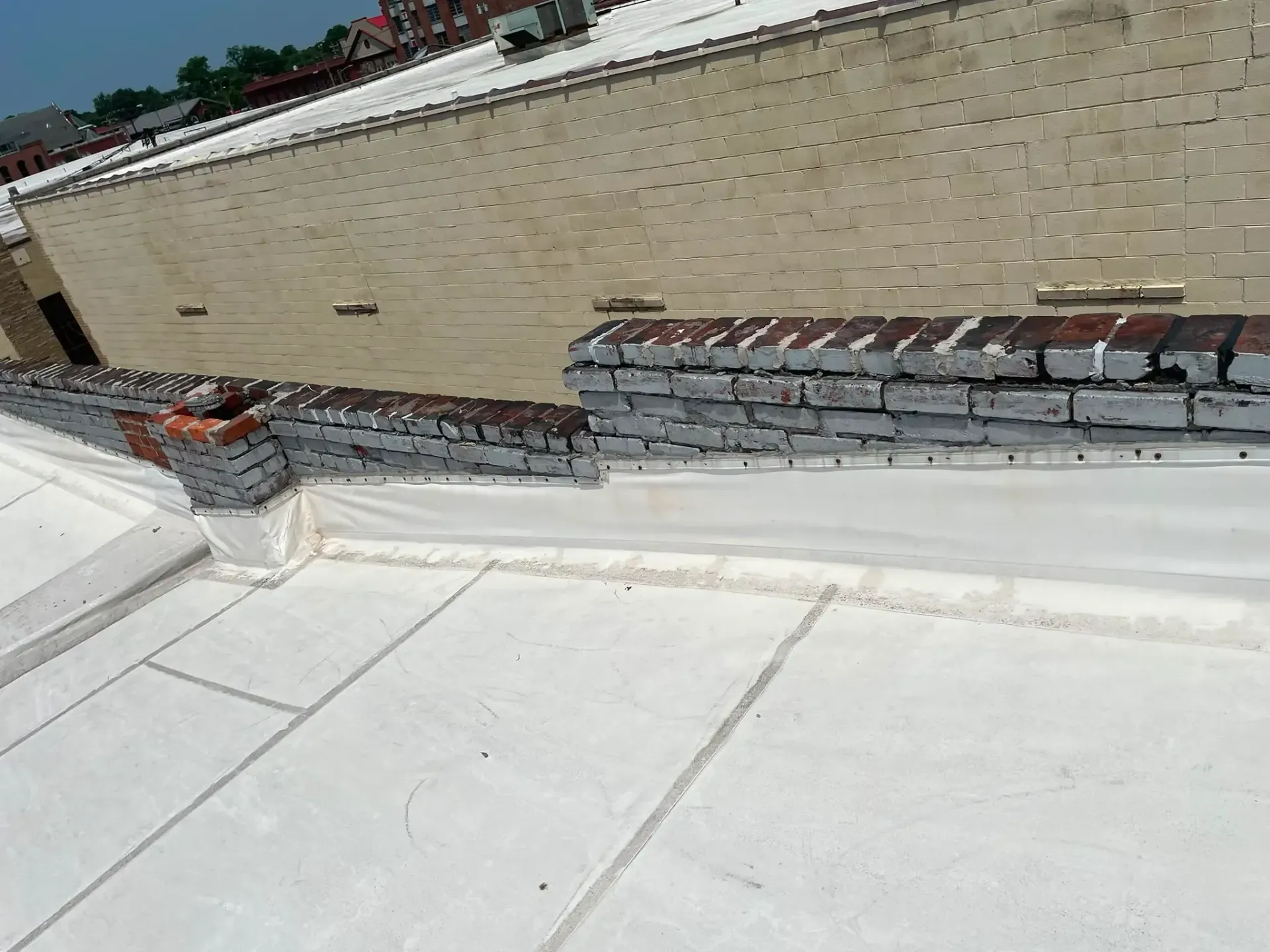 White rooftop with brick parapet and scattered construction materials along the edge