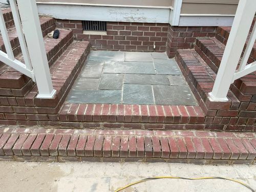 Brick steps and a small stone landing leading to a front porch entrance