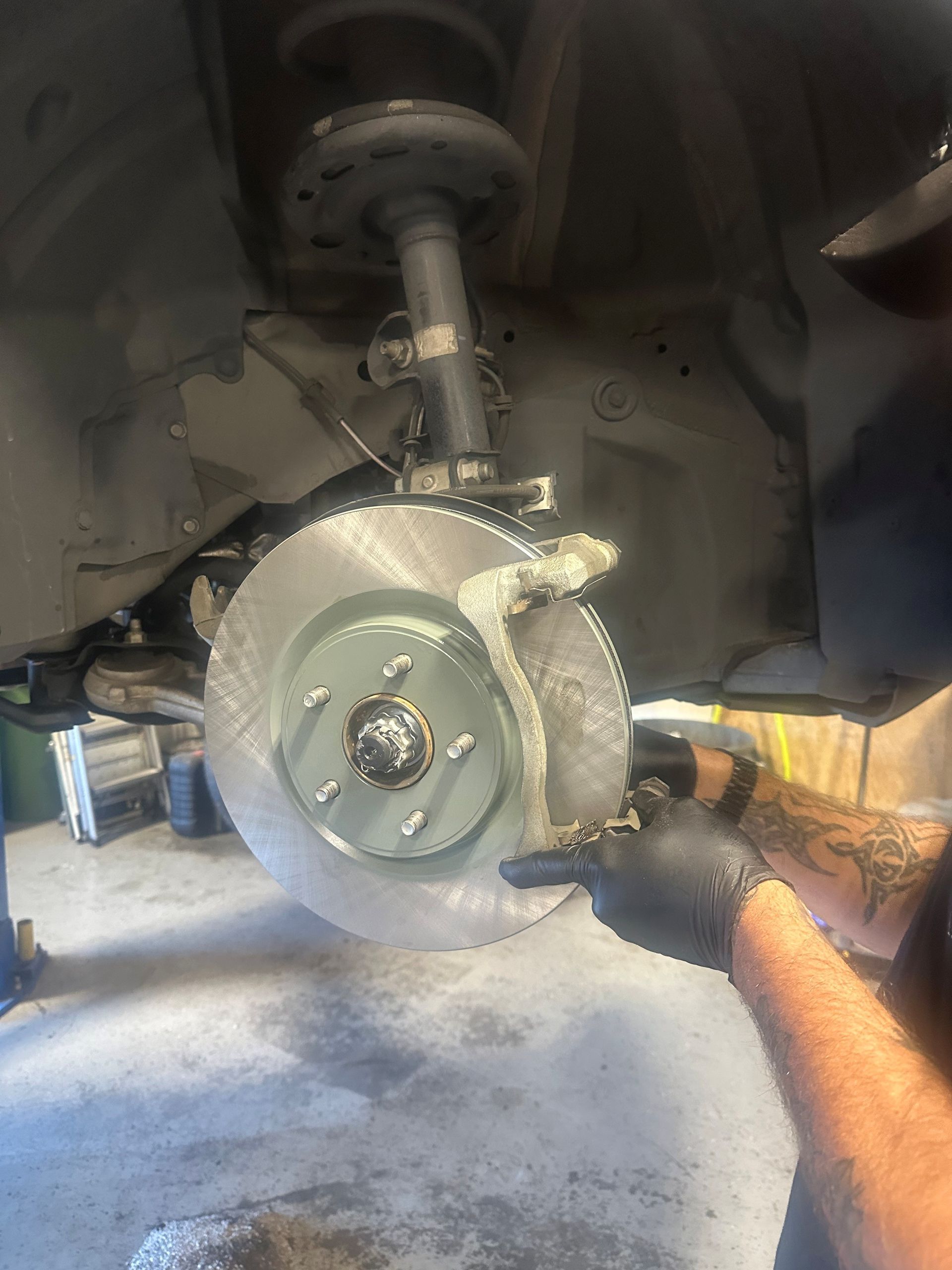 Car brake rotor being worked on; mechanic's hand holding tool near caliper and new rotor on the vehicle.