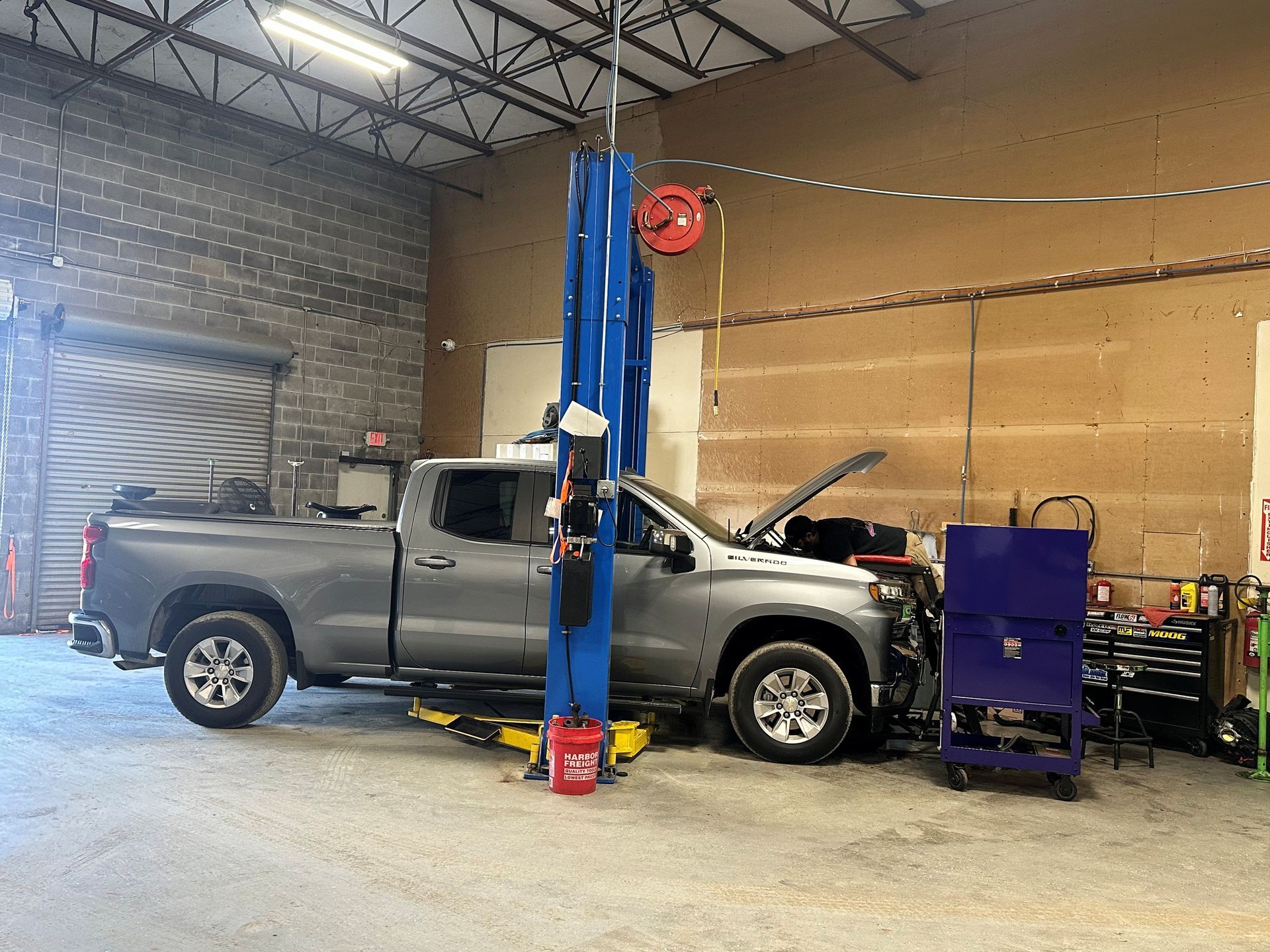 A gray pickup truck on a lift in a garage with open hood. Tools and equipment visible.