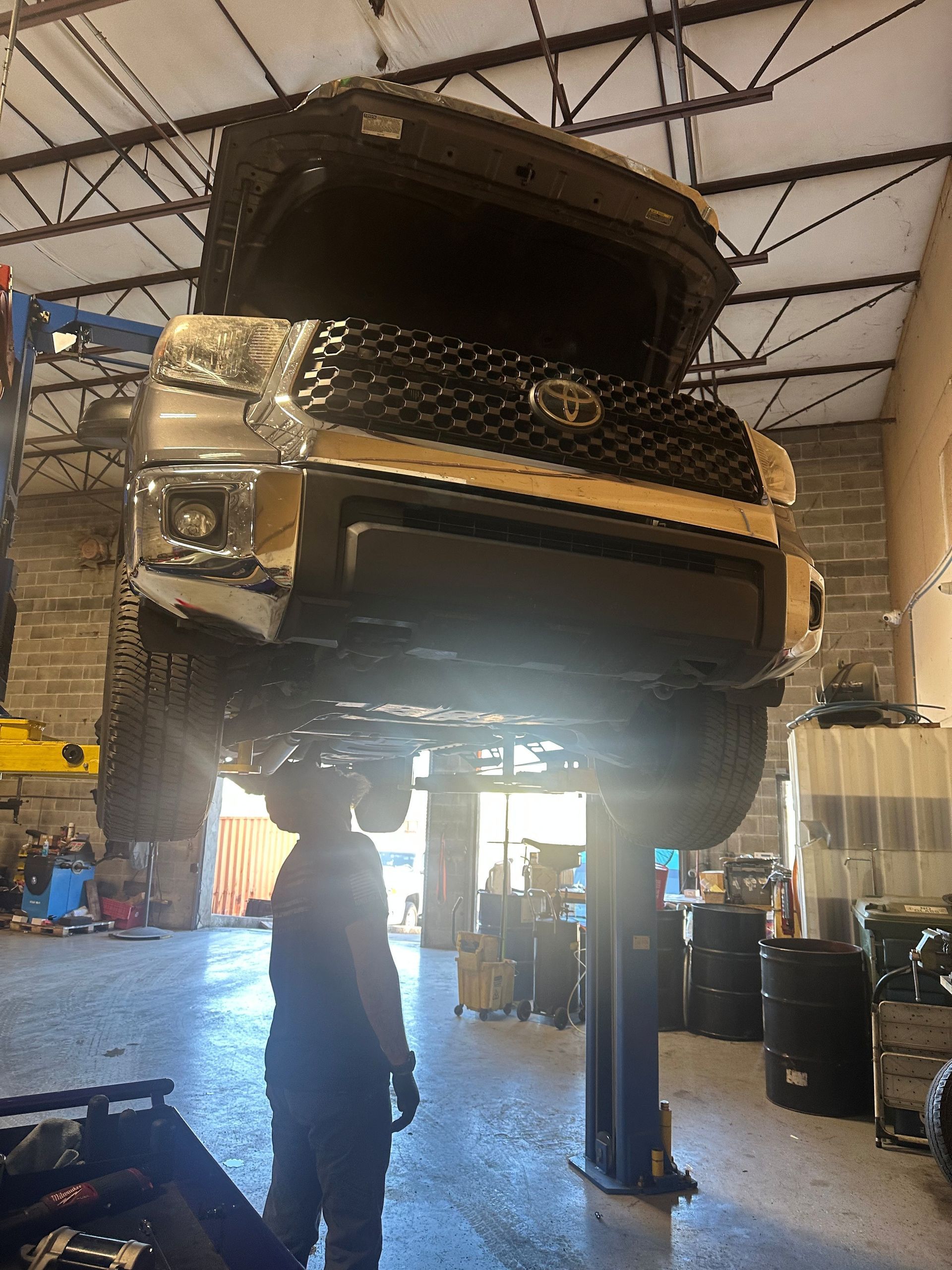 A truck raised on a lift in a repair shop, with a person standing underneath.