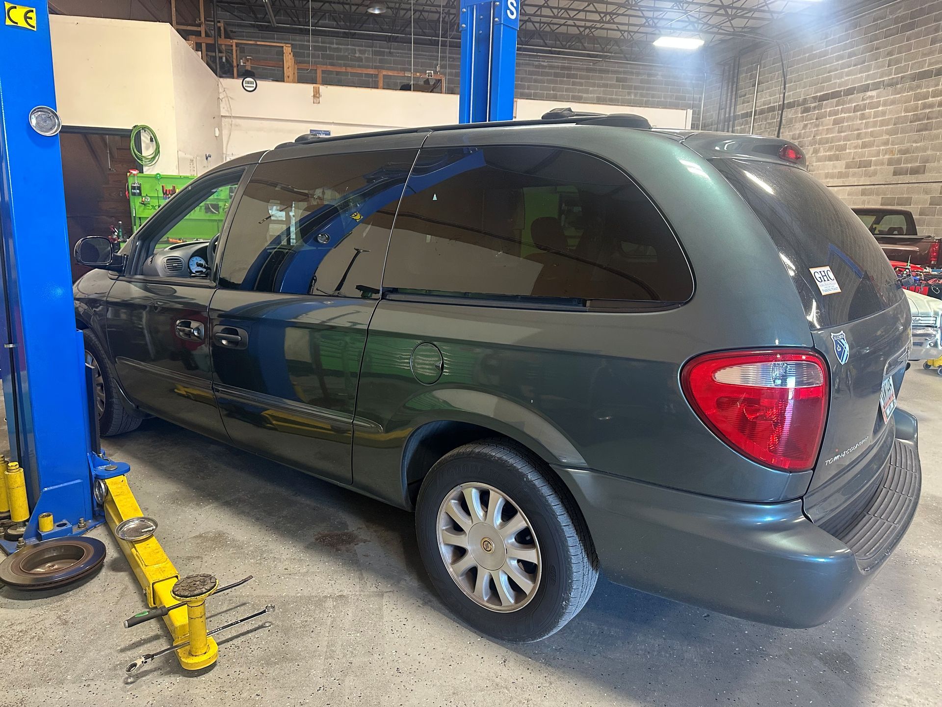 Green minivan in a garage, on a lift.