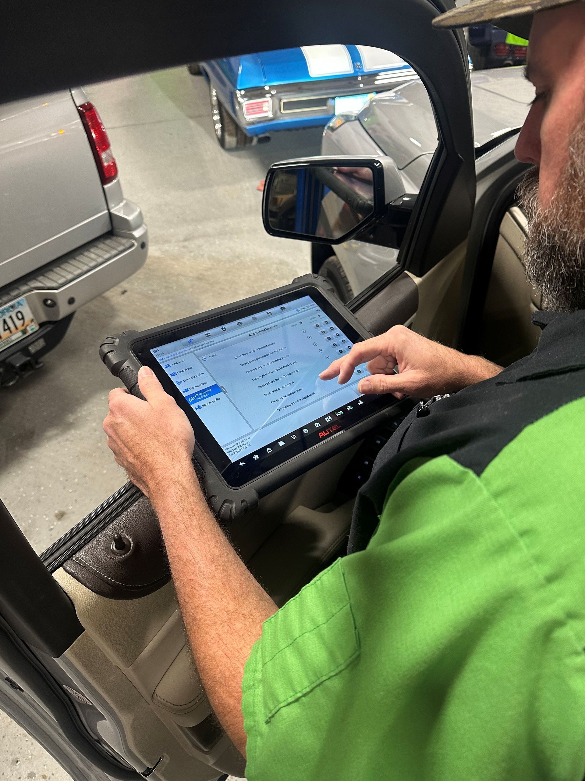 Mechanic uses tablet diagnostic tool inside a vehicle. Garage setting, green shirt, focused expression.