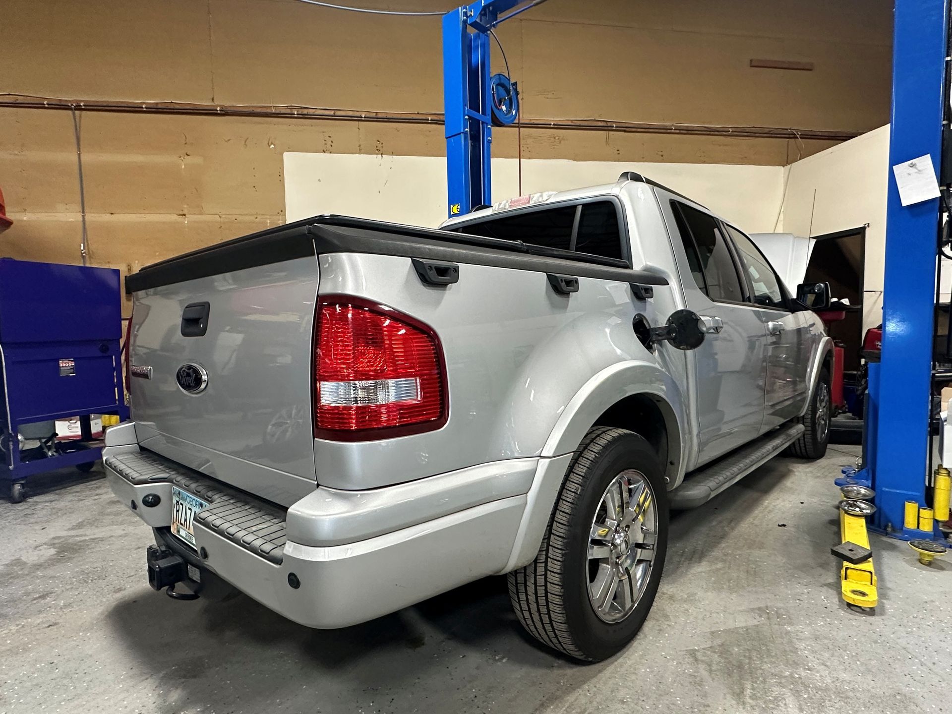 Silver Ford Explorer Sport Trac pickup truck in a garage, next to a blue lift.