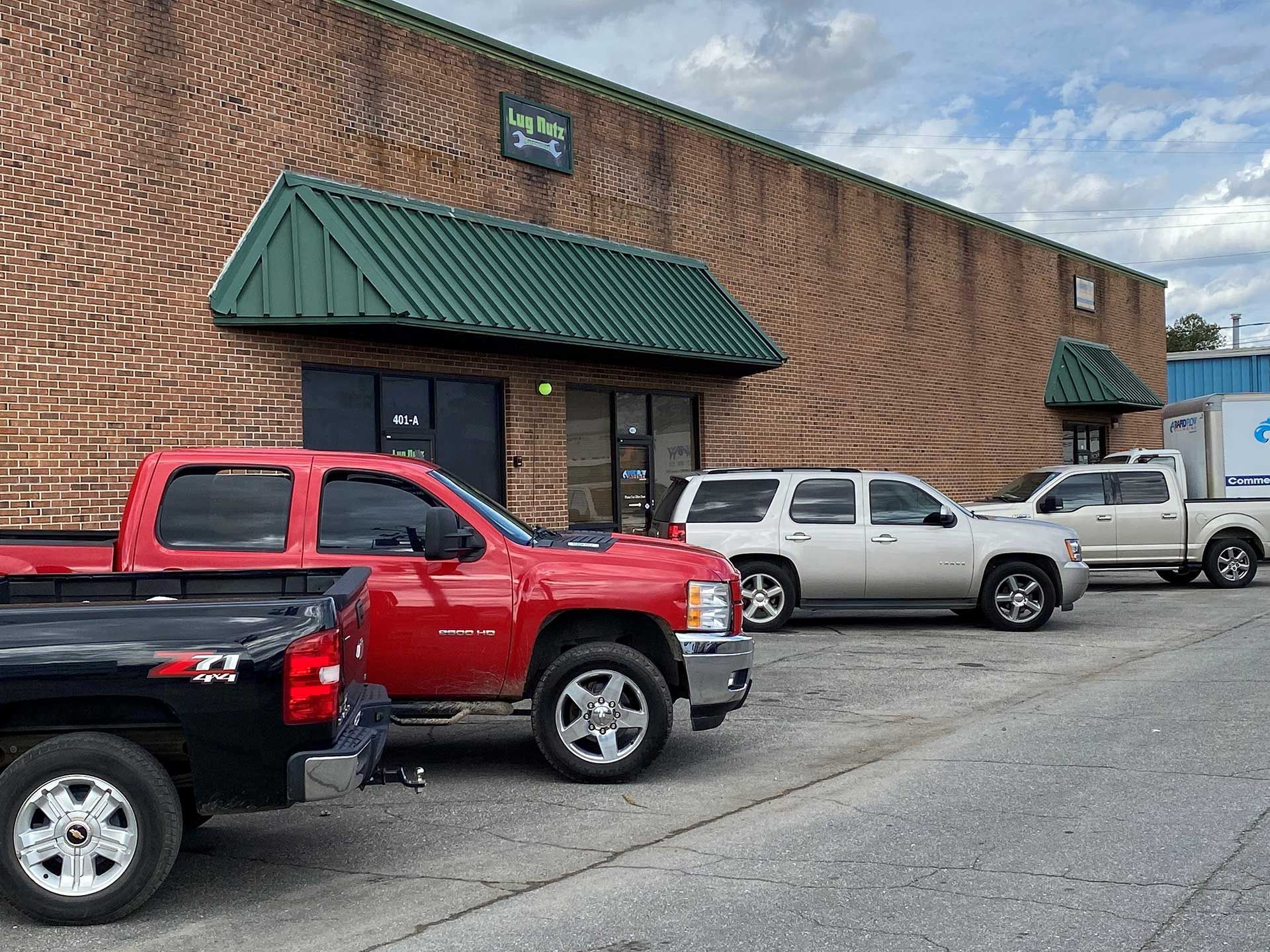 several trucks and SUVs parked in front of a brick building with green awnings