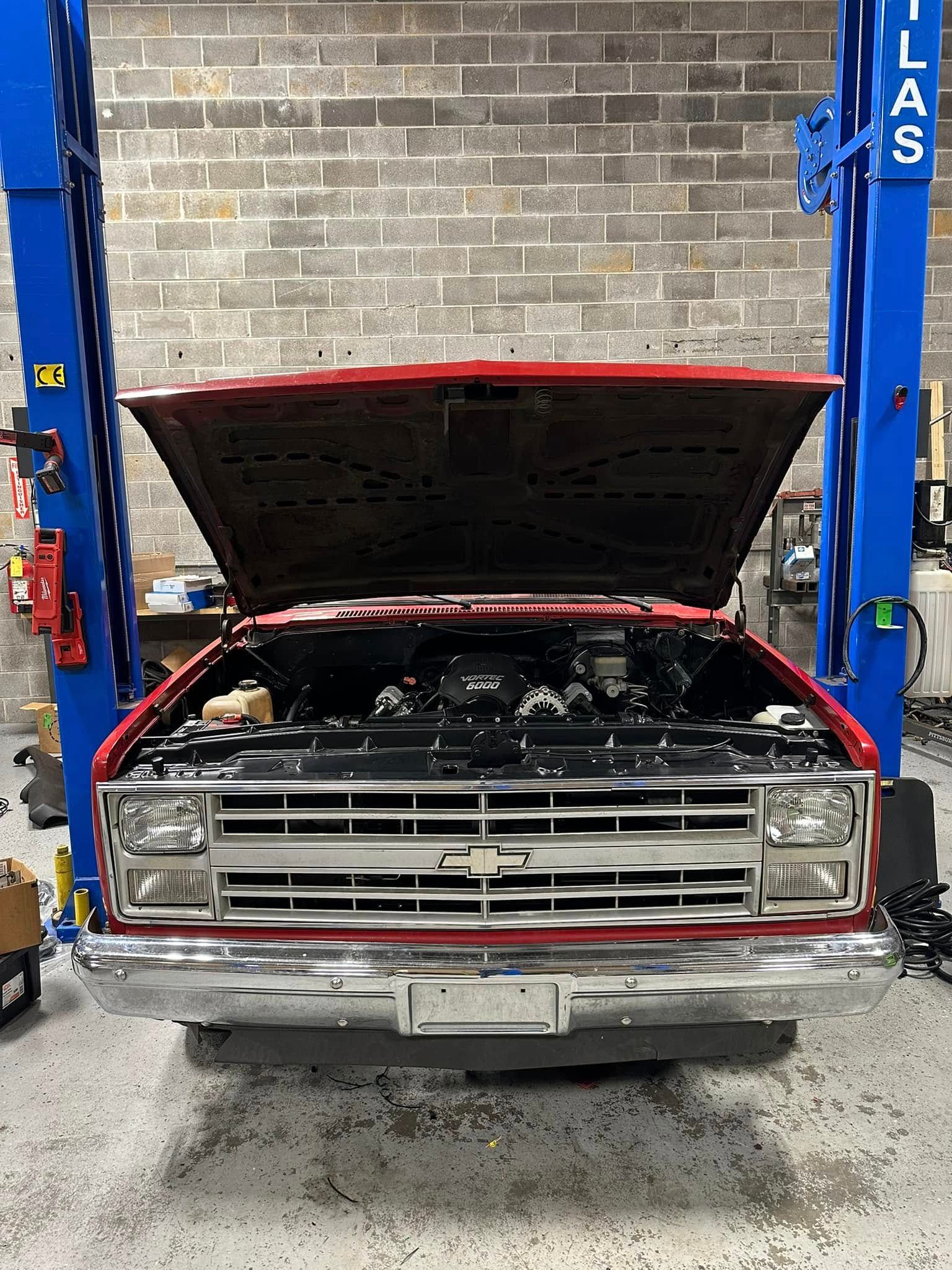 a red Chevrolet pickup truck on a lift with the hood open in a garage