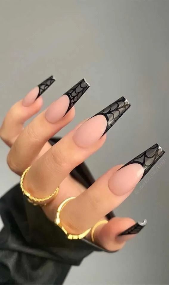 Hand with long, black and clear french tip nails, adorned with gold rings.