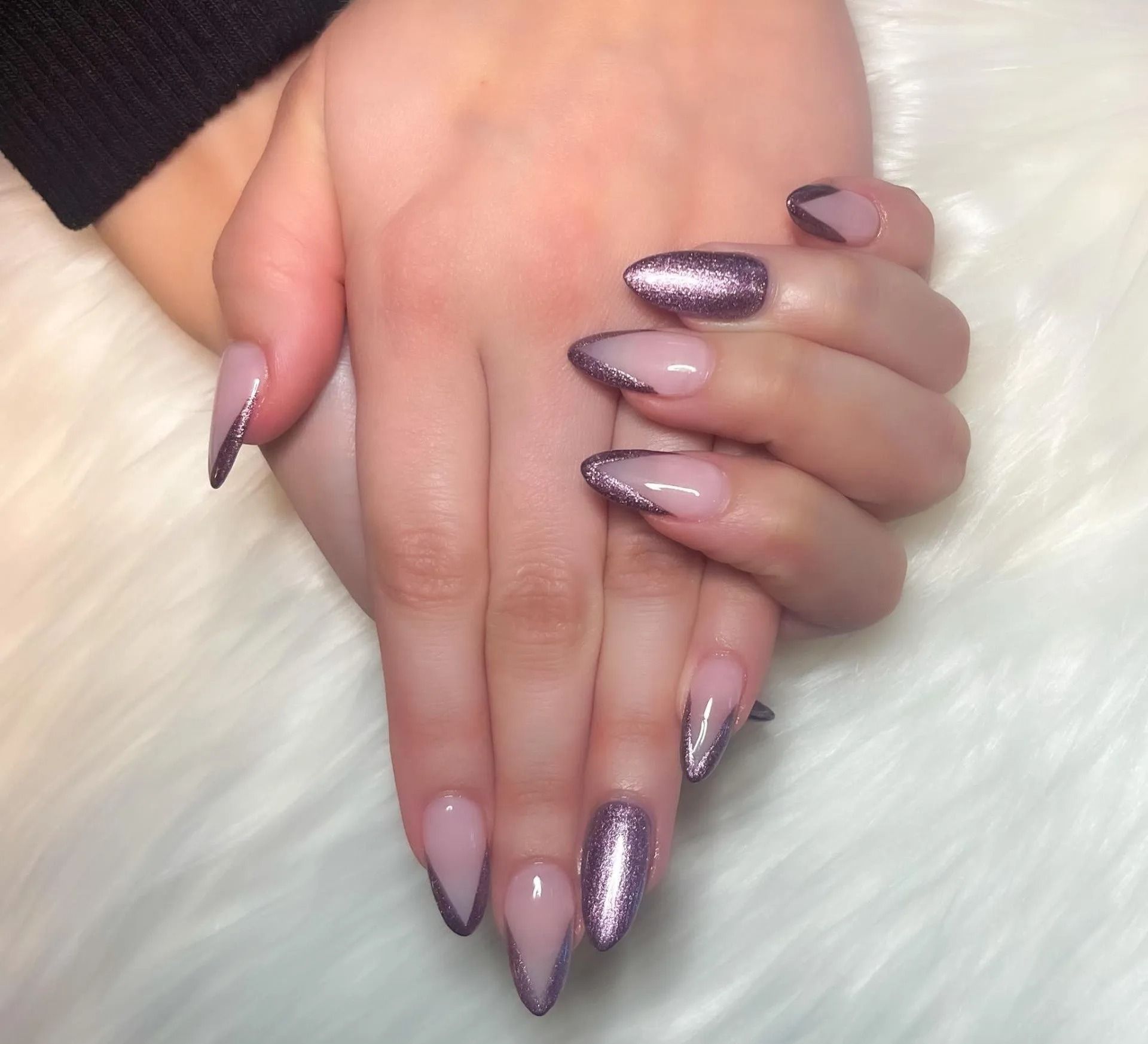 Hands with light pink, almond-shaped nails featuring sparkly purple glitter tips outlined in silver.