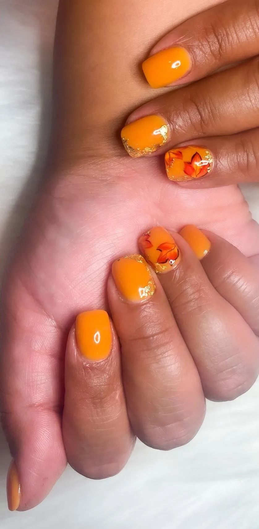 Hands with orange nails, some with gold glitter and autumn leaf designs.