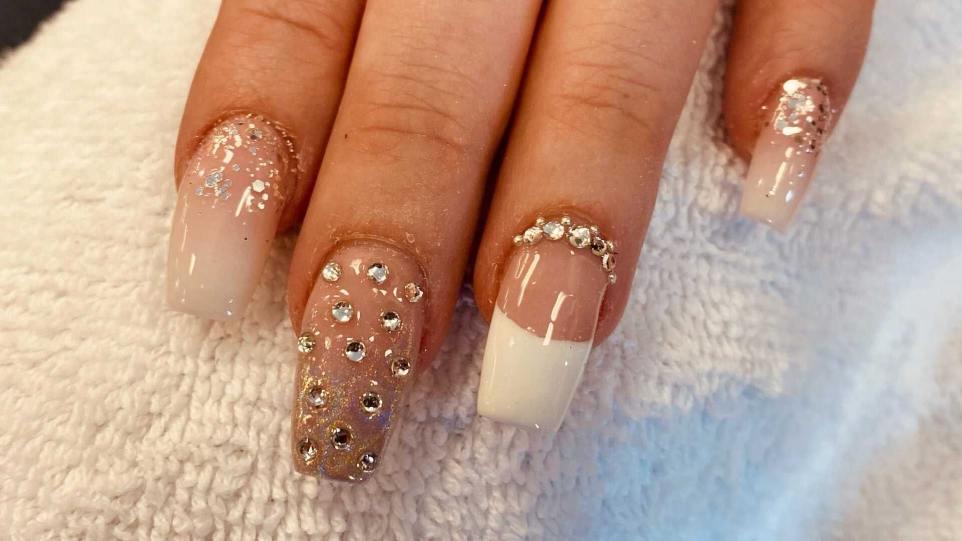 Close-up of hand with long, decorated nails: ombre, white French tip, and crystal embellishments on a white towel.