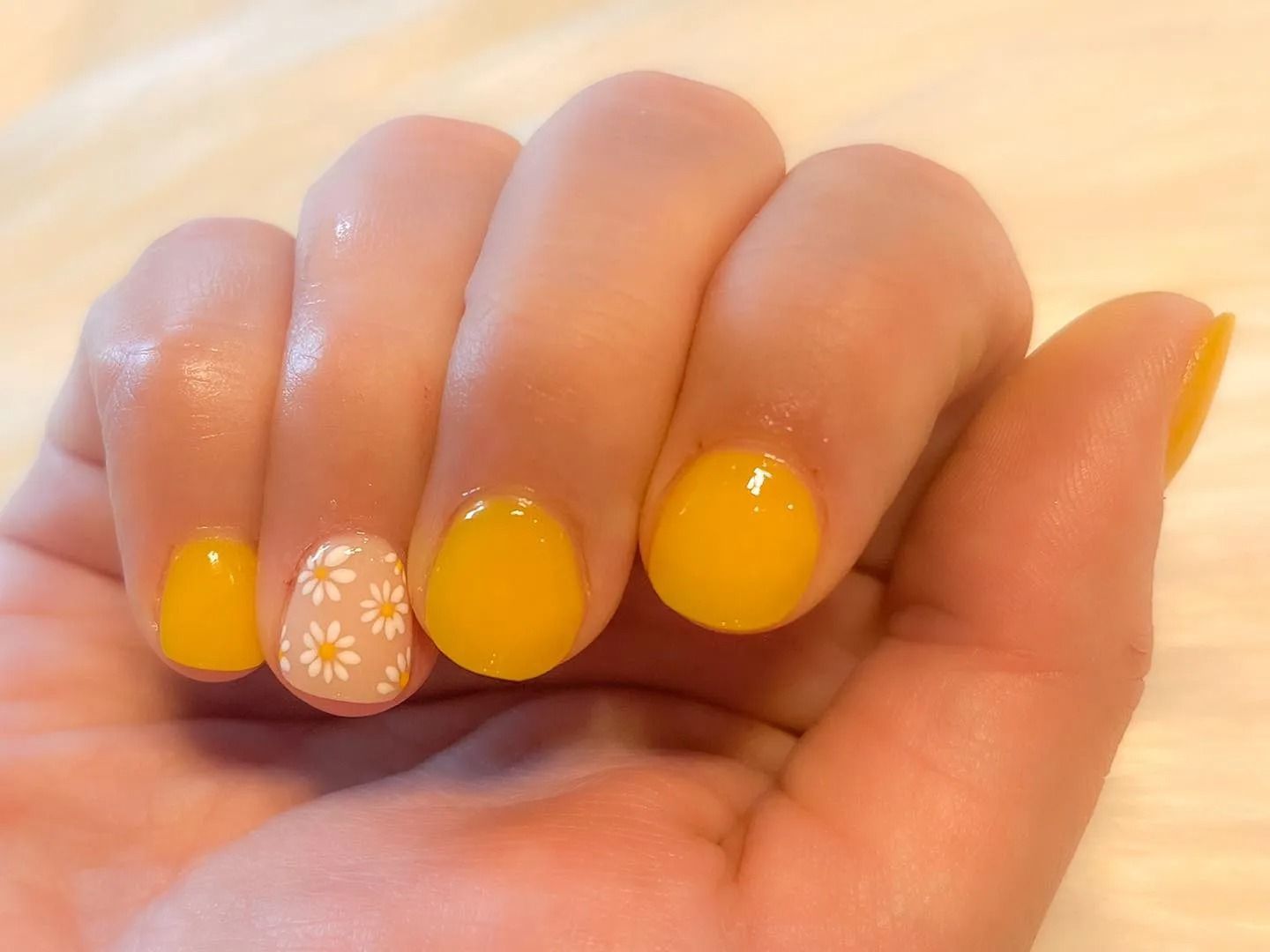 Hand with yellow and daisy print nail polish on a light-colored surface.