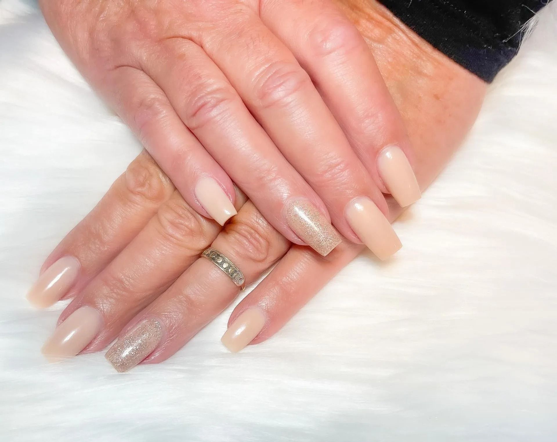 Hands with pale, square-shaped acrylic nails. One nail on each hand is covered in glitter.