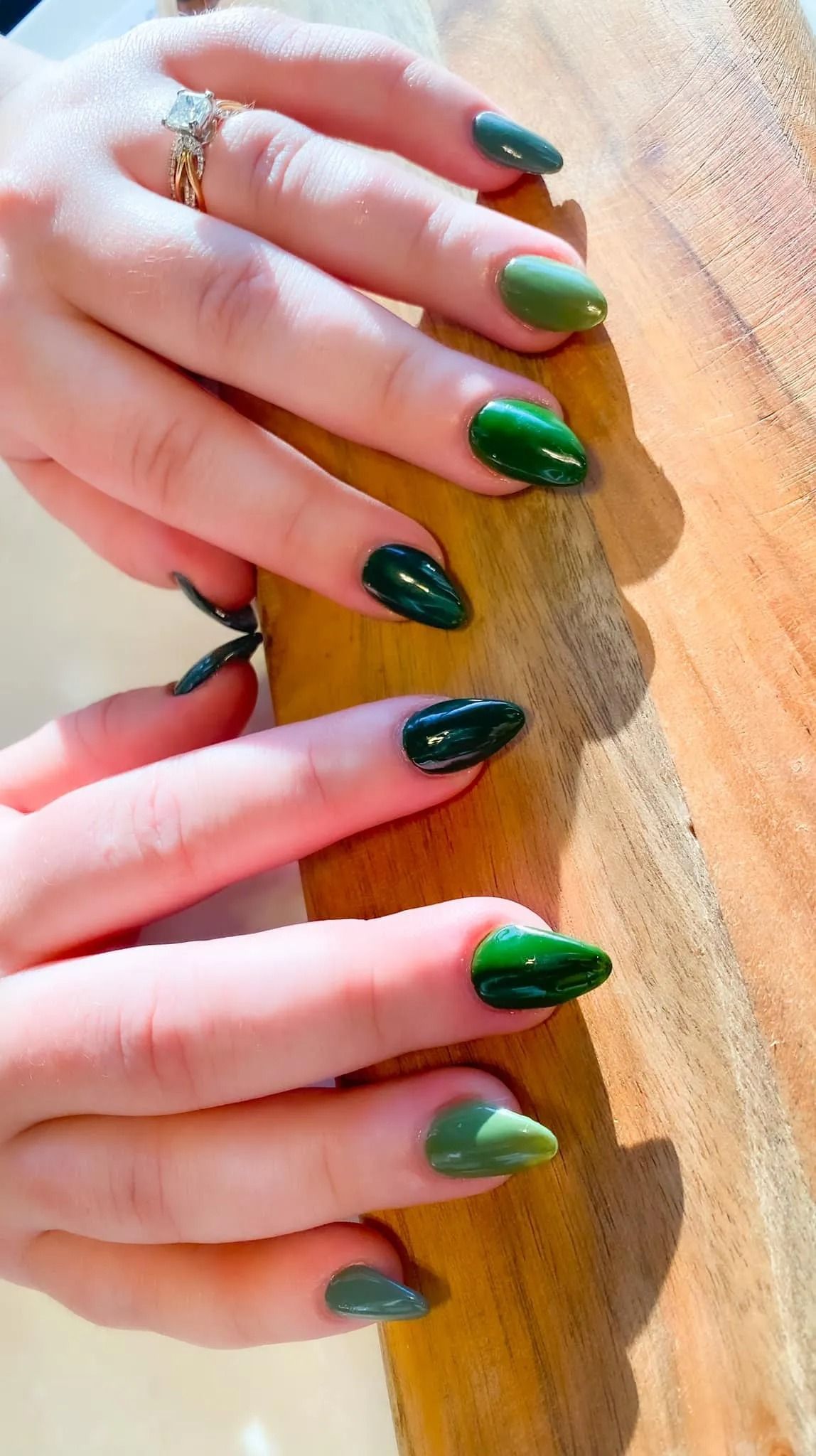 Hands with green almond-shaped nails resting on a wooden surface. Ring on finger.