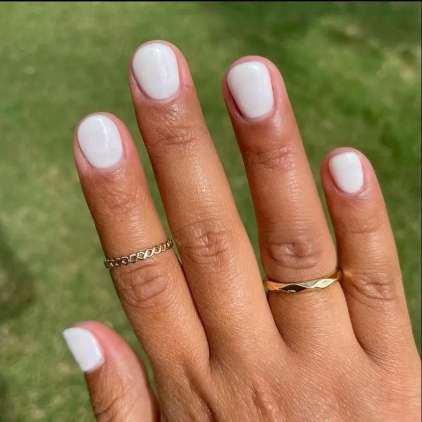 Hand with white nail polish and gold rings, outdoors.
