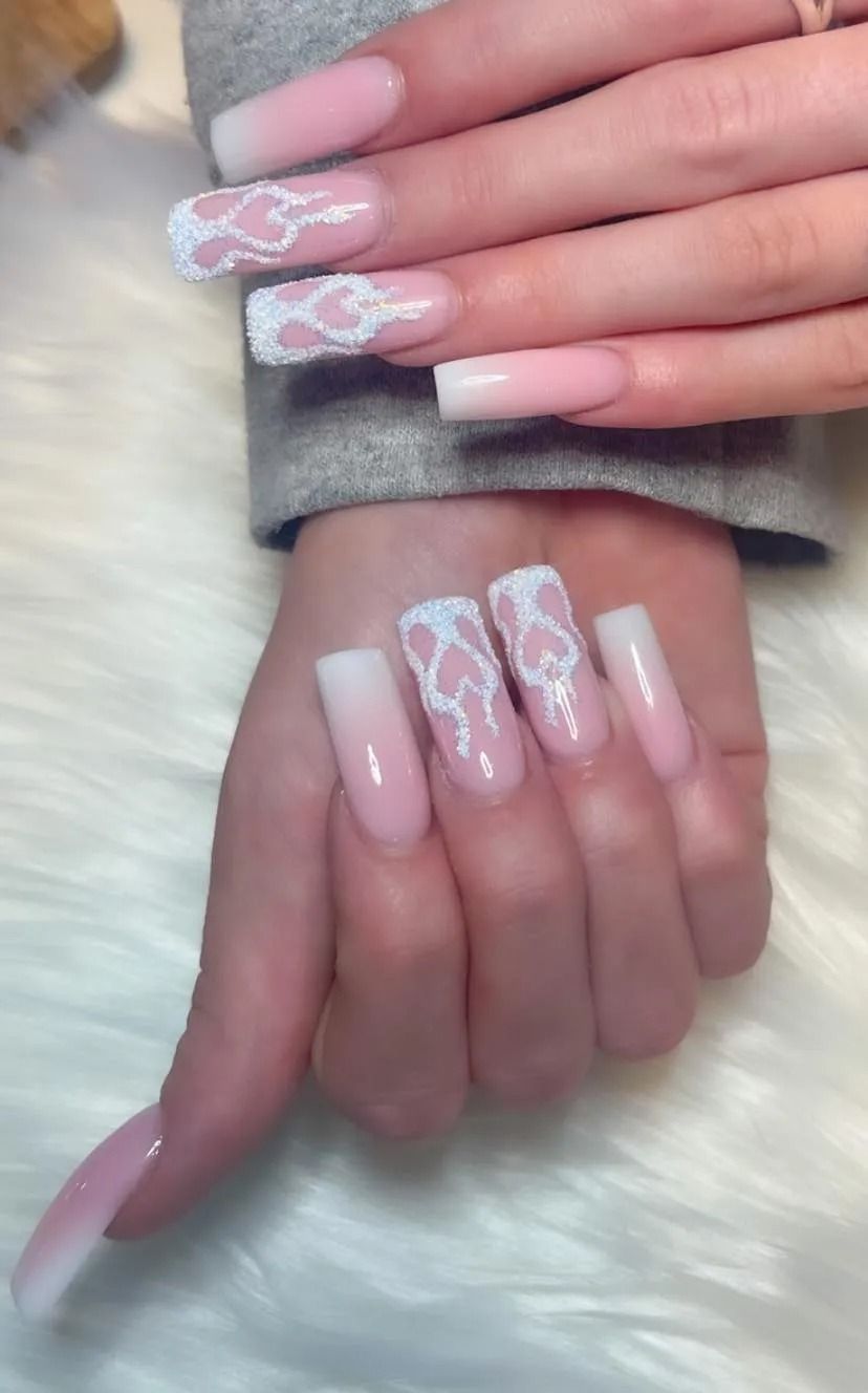 Hands with long, square-shaped acrylic nails. The ombre pink nails have white lace heart designs on some.