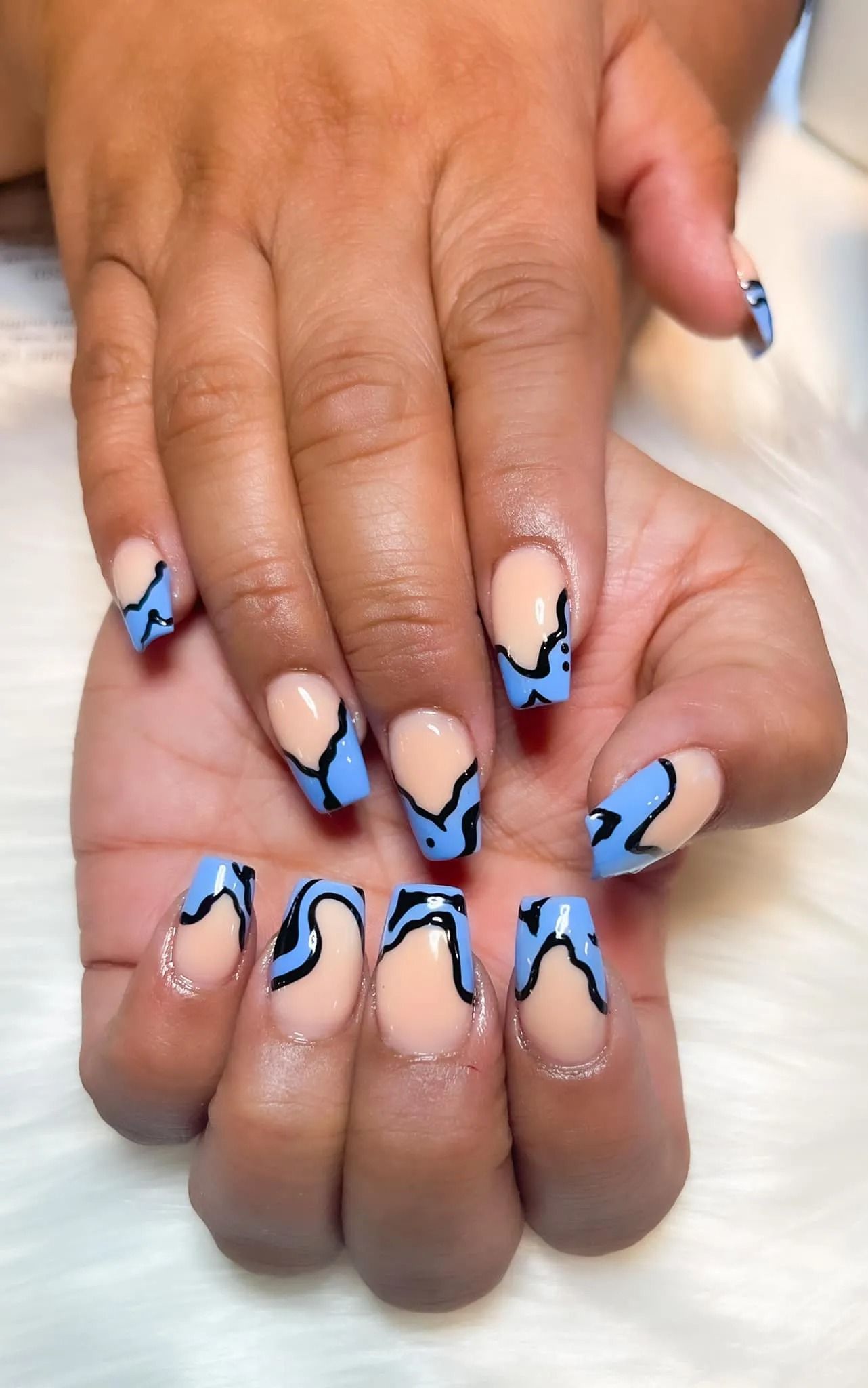 Close-up of a person's manicured hand. Light blue nails with black wavy designs.