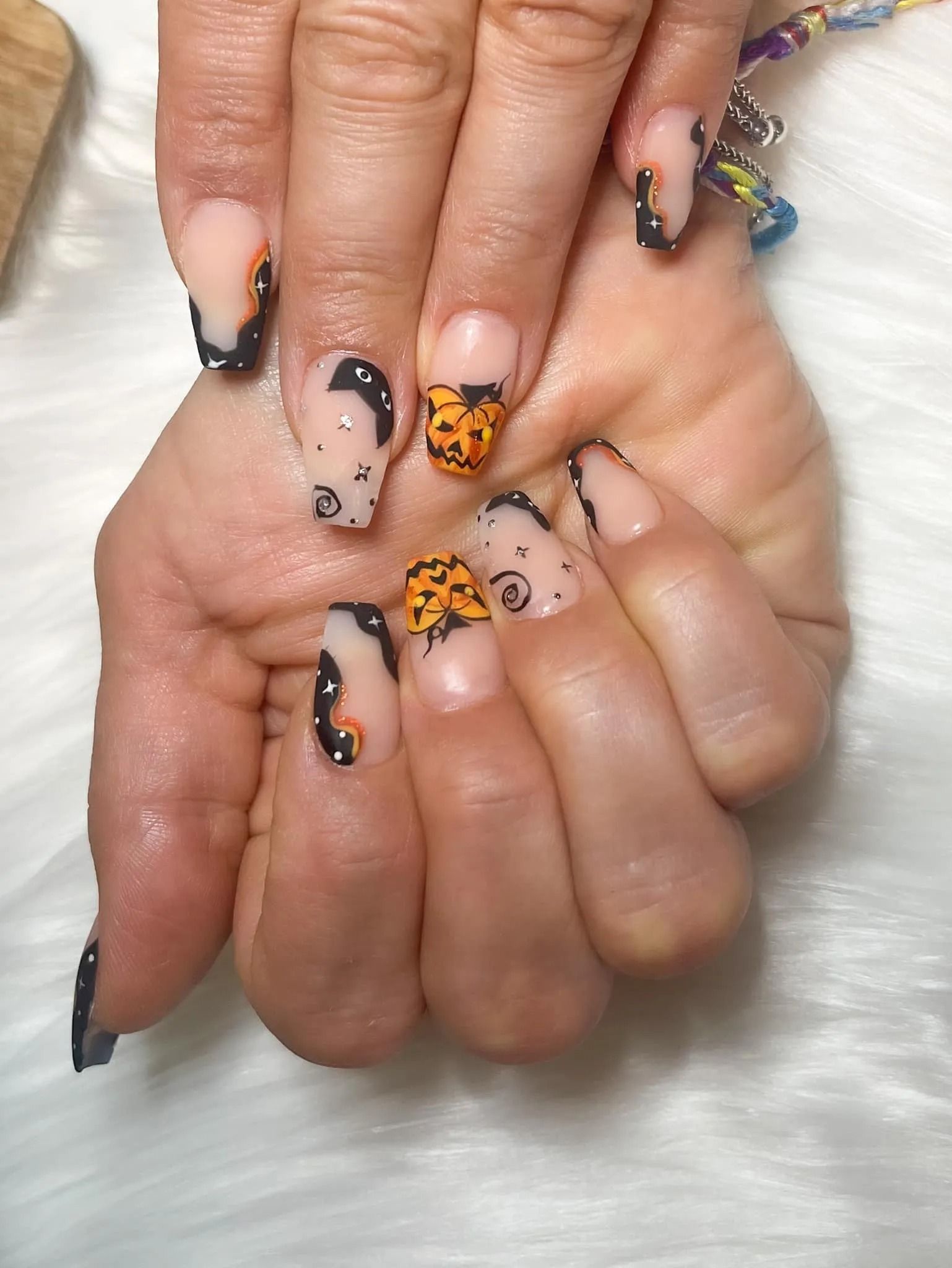 Hand with long, square nails featuring Halloween-themed nail art. Black tips, jack-o'-lanterns, and black moon shapes.