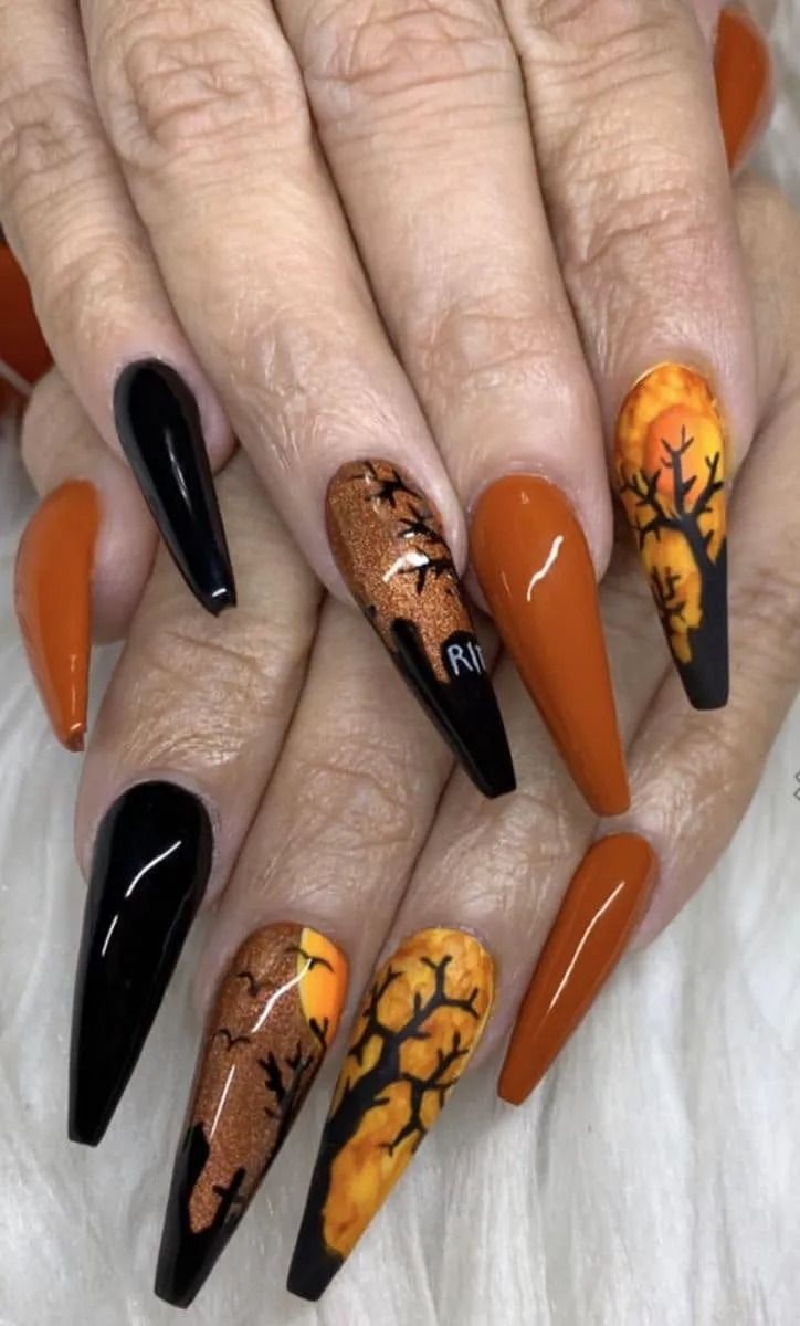 Halloween-themed nail art. Long, coffin-shaped nails with black, orange, and glitter designs, including trees and bats.