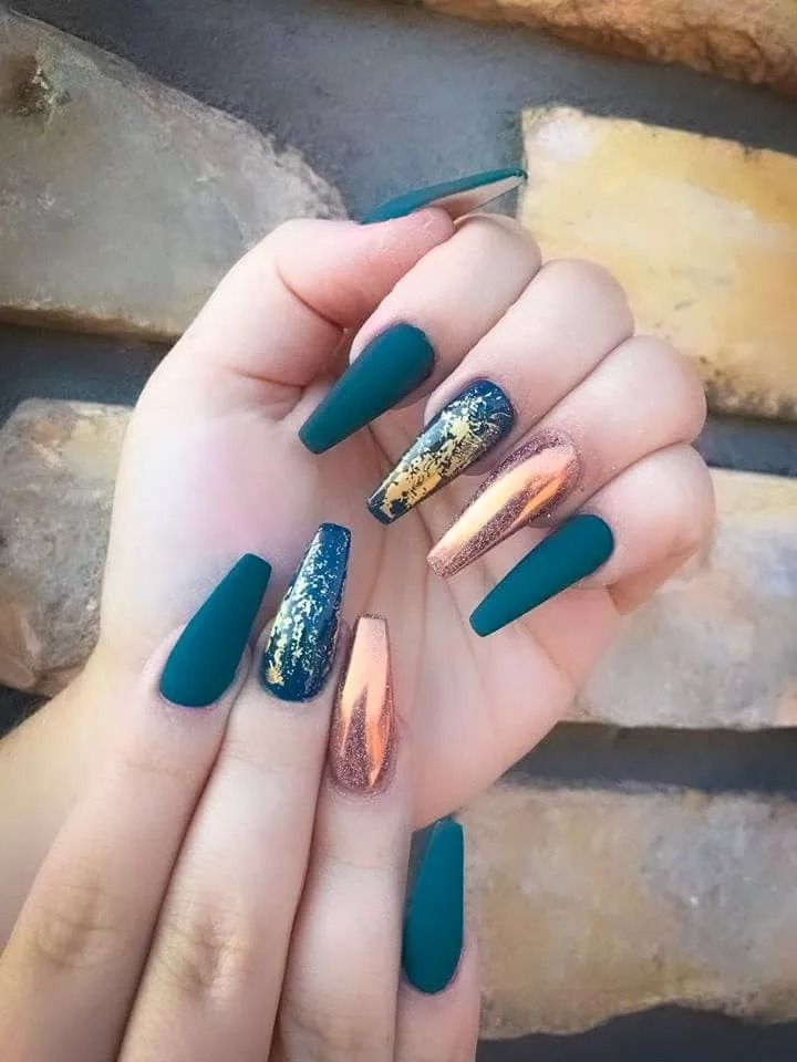 Green matte coffin-shaped nails, some with gold and copper accents, against a stone background.