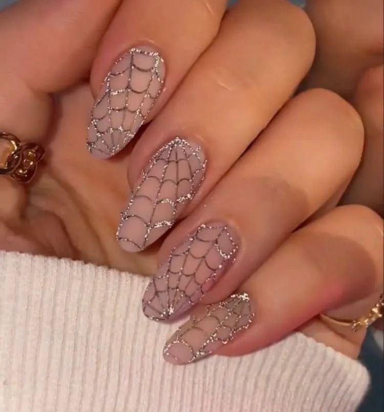 Hand with oval nails, each painted with a sheer nude base and silver glitter spiderweb design.