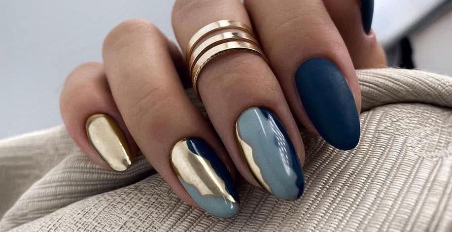 Close-up of a hand with oval-shaped nails, painted gold, teal, and navy, with a gold ring.
