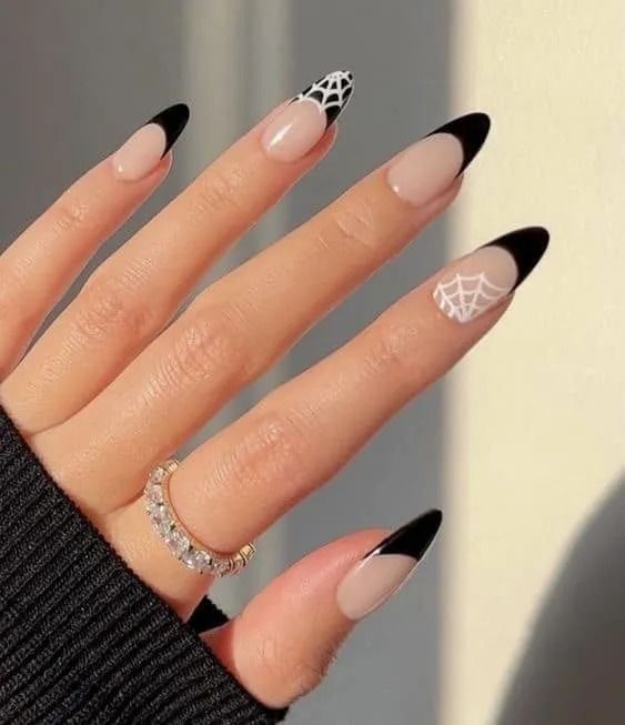 Hand with long, almond-shaped nails. Black tips, French manicure. One nail has white spiderweb. Sparkling ring.