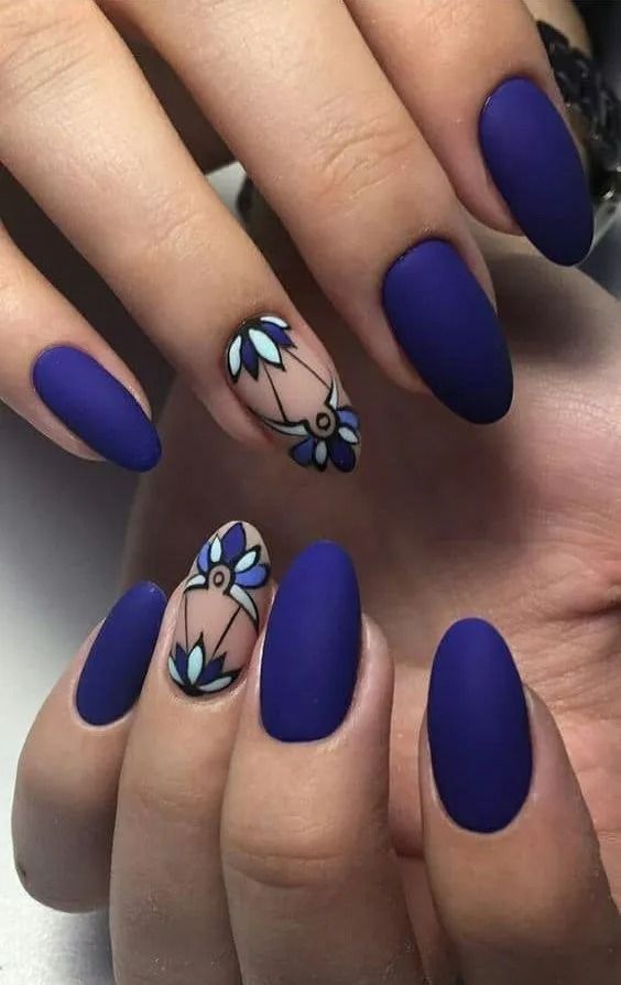 Matte blue almond-shaped nails with floral accent nails in a close-up shot.