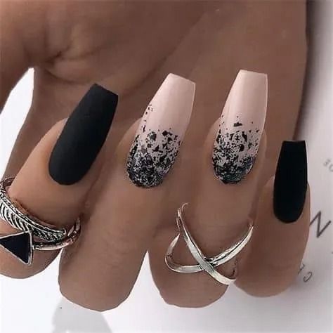 Hand with matte black and nude coffin-shaped nails, two with black glitter, and silver rings.