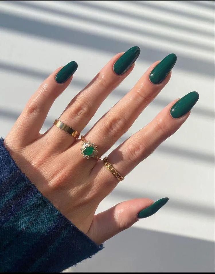 Hand with long, dark green oval nails, rings.