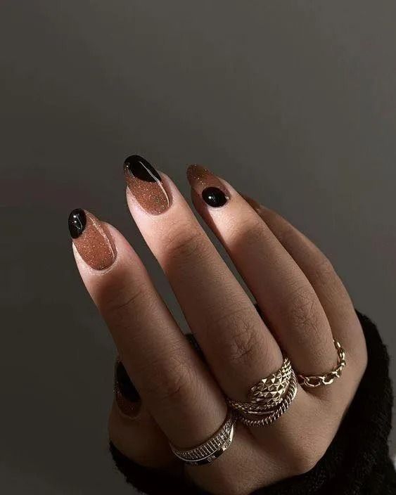 Hand with brown and black French tip nails, adorned with rings.