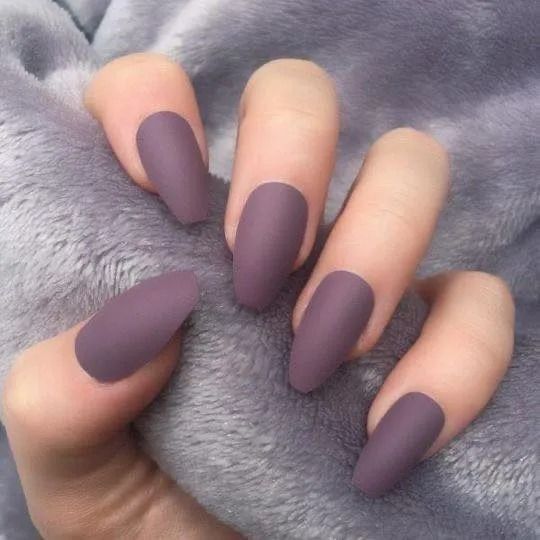 Hand with five matte purple oval-shaped nails against a fuzzy gray background.