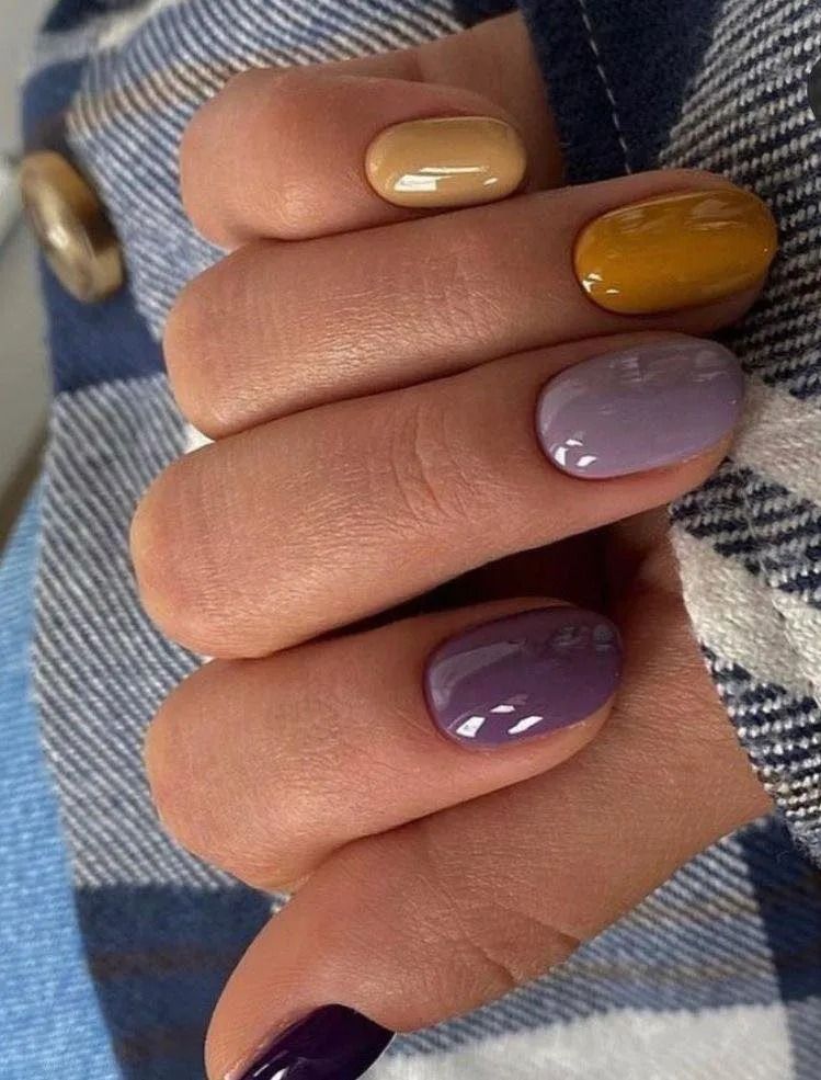 Hand with five nails painted in varying shades of tan, yellow, lavender, and purple.