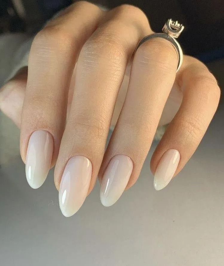 Hand with almond-shaped nails painted light pink, wearing a diamond ring.