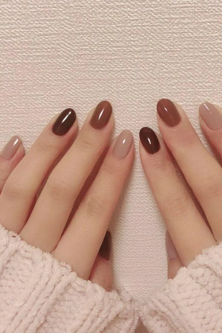 Hands with oval-shaped nails painted in shades of brown and beige.