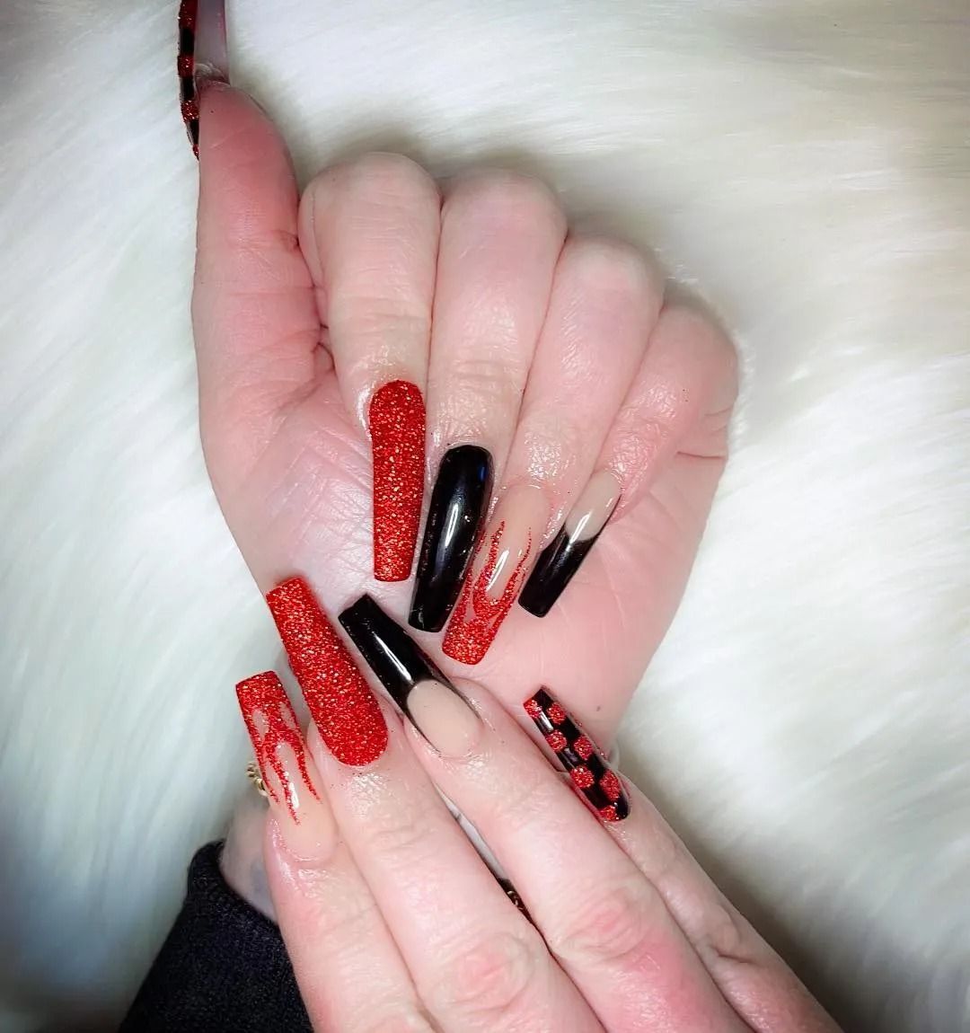 Long coffin-shaped nails with red glitter, black polish, and ombre designs against a white background.